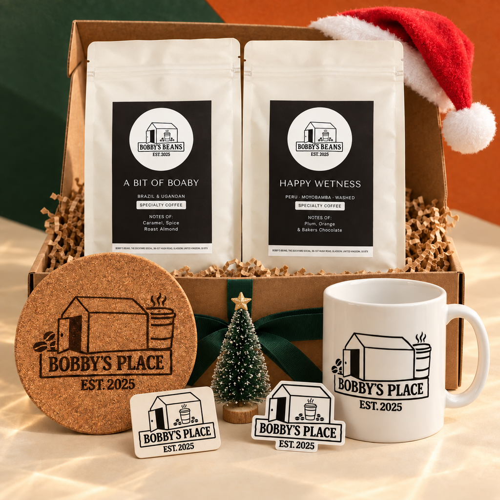 An Xmas Box Of Boaby with A Bit of Boaby and Happy Wetness coffee, Bobby's Place mug, giant cork coaster, magnet and sticker, styled with a Santa hat and miniature Christmas tree.