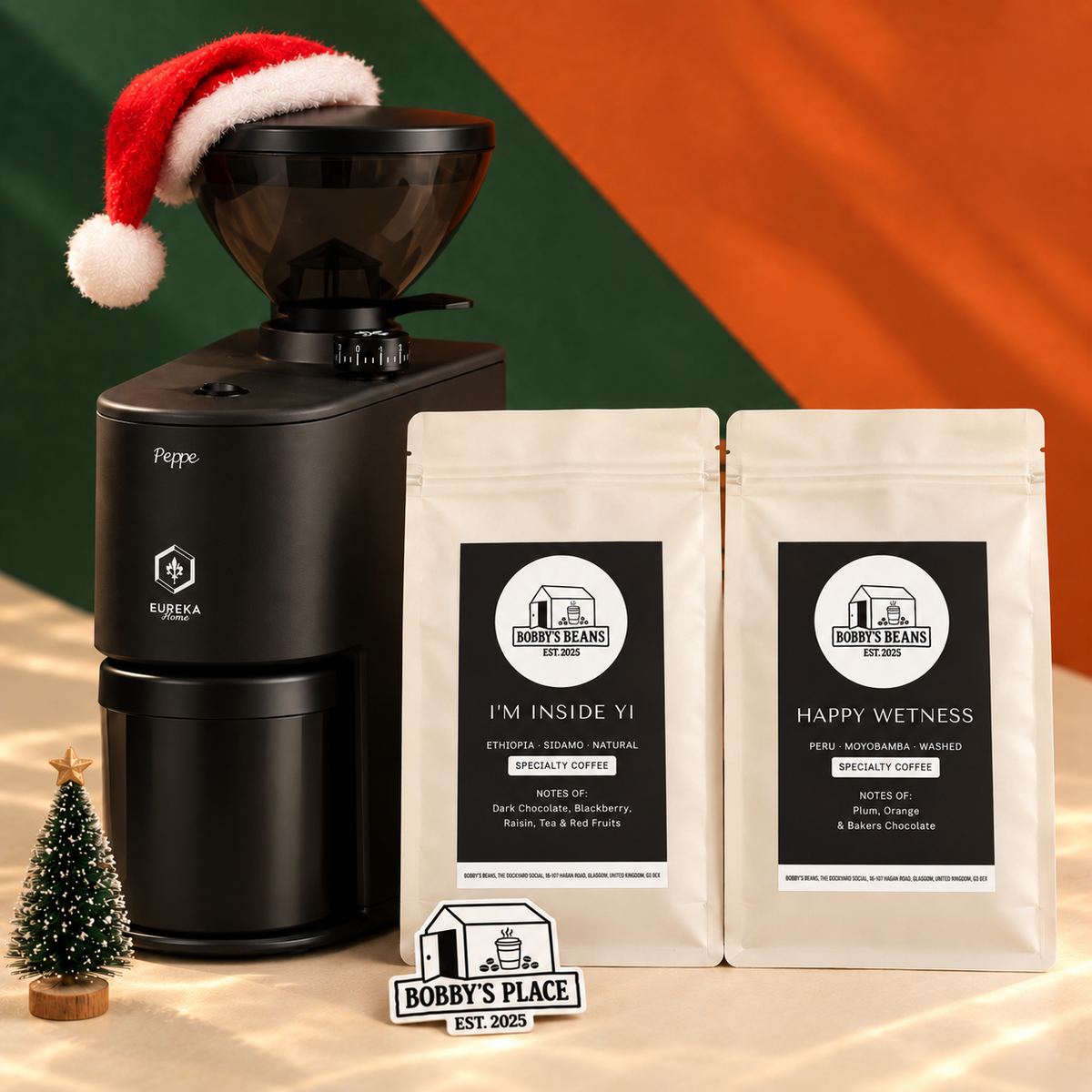 The Big One with a black Eureka Peppe 50 grinder, I'm Inside Yi coffee and Happy Wetness coffee, styled with a Santa hat and miniature Christmas tree. Includes a Bobby's Place glow in the dark sticker.